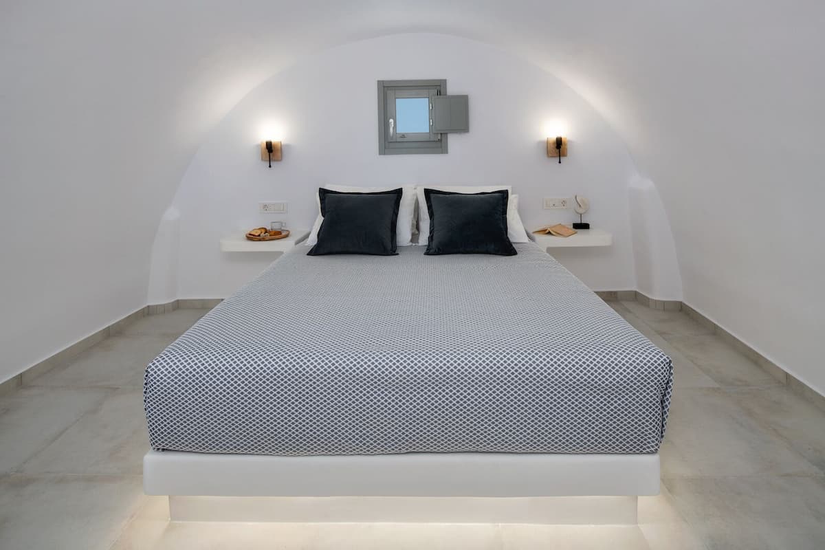 Un dormitorio moderno con una cama, dos mesitas de noche, una lámpara de pared y un ventanal pequeño.