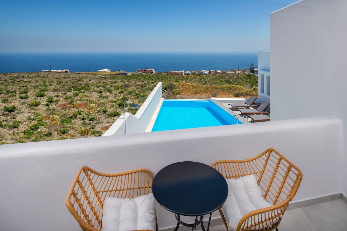 Un balcón con piscina, sillas de mimbre y una mesa con vistas al paisaje costero.