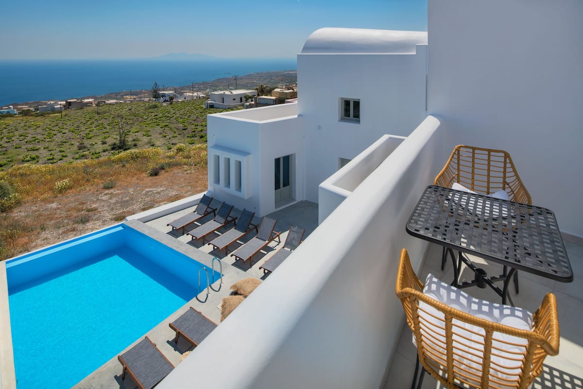 Zona de piscina en la azotea con sillones y una mesa, con vistas a un paisaje costero.