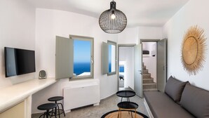 A modern living room with a sofa, a TV, a dining area with stools, and a view of the sea through open doors.