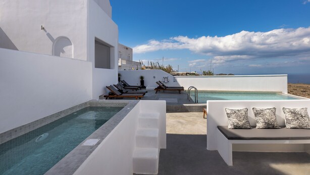 A modern outdoor pool area with a white building, lounge chairs, and a seating area with cushions.