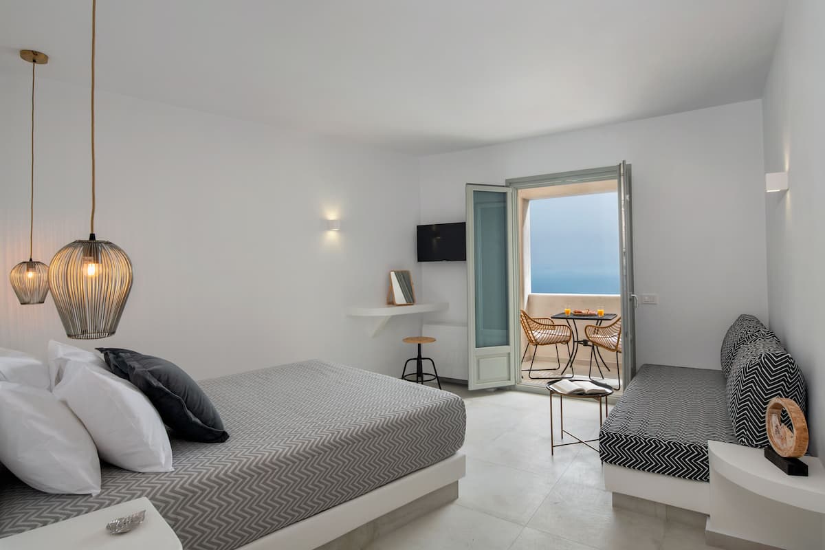 Un dormitorio moderno con cama, mesitas de noche, televisor y vista al mar.