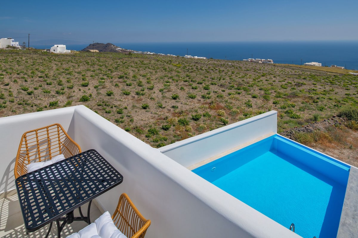 Zona de piscina con una mesa y sillas, con vistas a un paisaje de vegetación escasa y edificios al fondo.