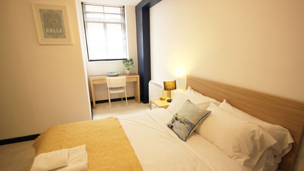 A neatly arranged bedroom with a bed, bedside table, lamp, and a desk with a chair. - Great Location Shoreditch Spitalfields (London)