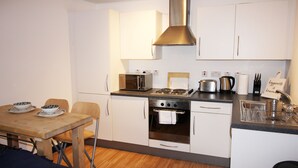 A compact kitchen with white cabinets, a stove, a microwave, and a sink. - Great Location Shoreditch Spitalfields (London)