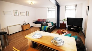 A modern living room with a wooden dining table, black leather sofa, and a flat-screen TV. - Great Location Shoreditch Spitalfields (London)