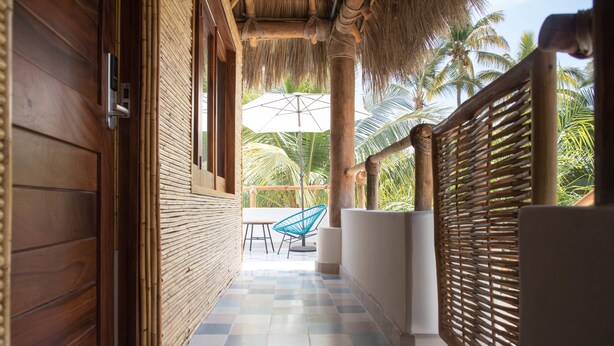 A corridor with a checkered floor, wooden walls, and a thatched roof. - PAL.MAR Hotel Tropical (San Francisco)
