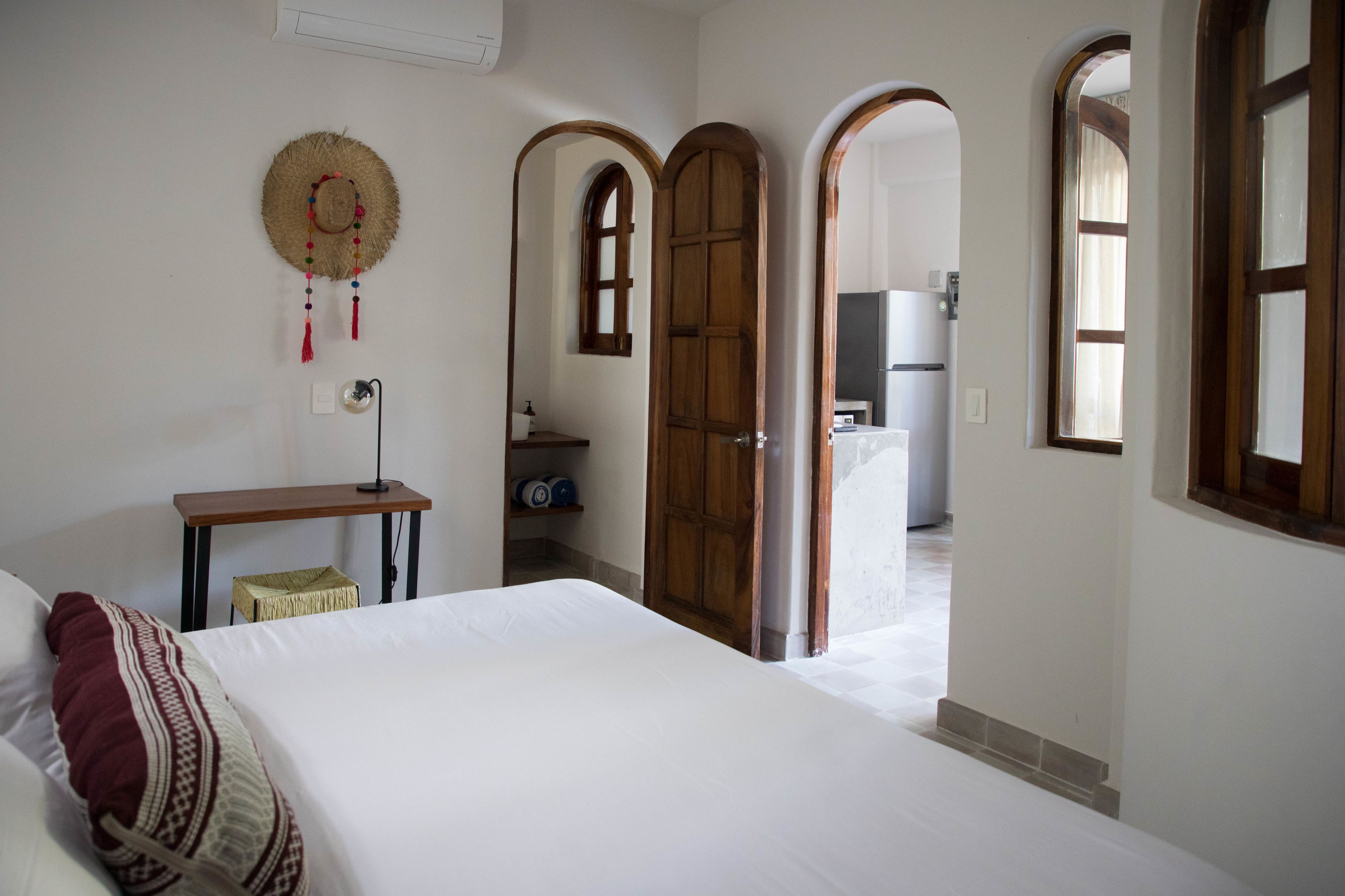 Une chambre avec un lit, un bureau et une armoire. Une porte donne accès à un espace cuisine.
