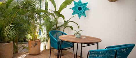 A patio with a round wooden table, two blue chairs, and a potted plant.
