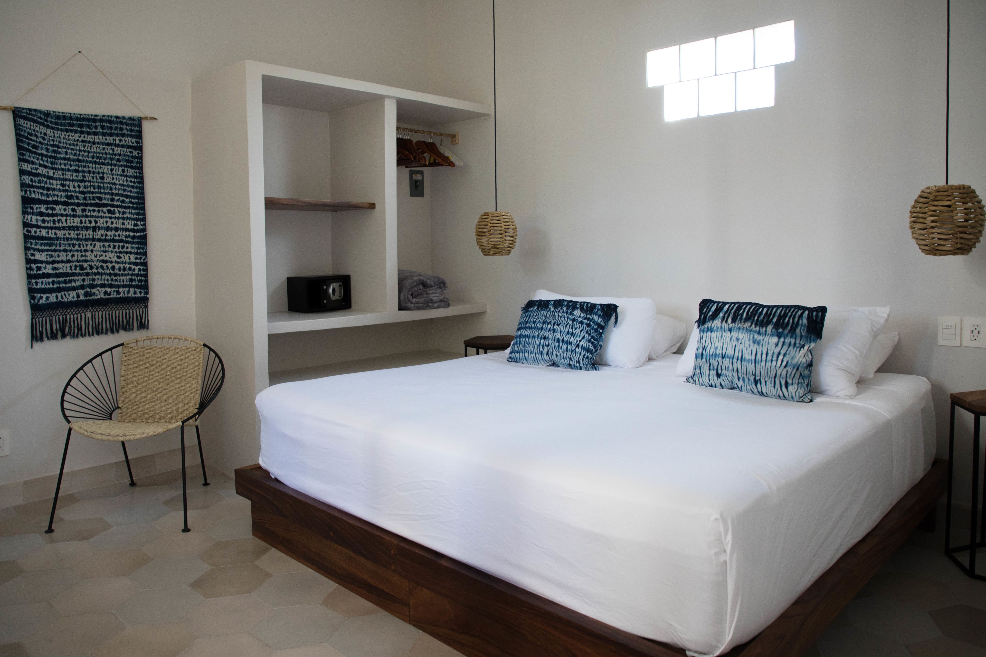Un dormitorio con una cama grande, una silla, un armario y una lámpara colgante.