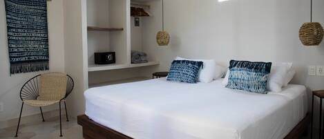 Un dormitorio con una cama grande, una silla, un armario y una lámpara colgante.