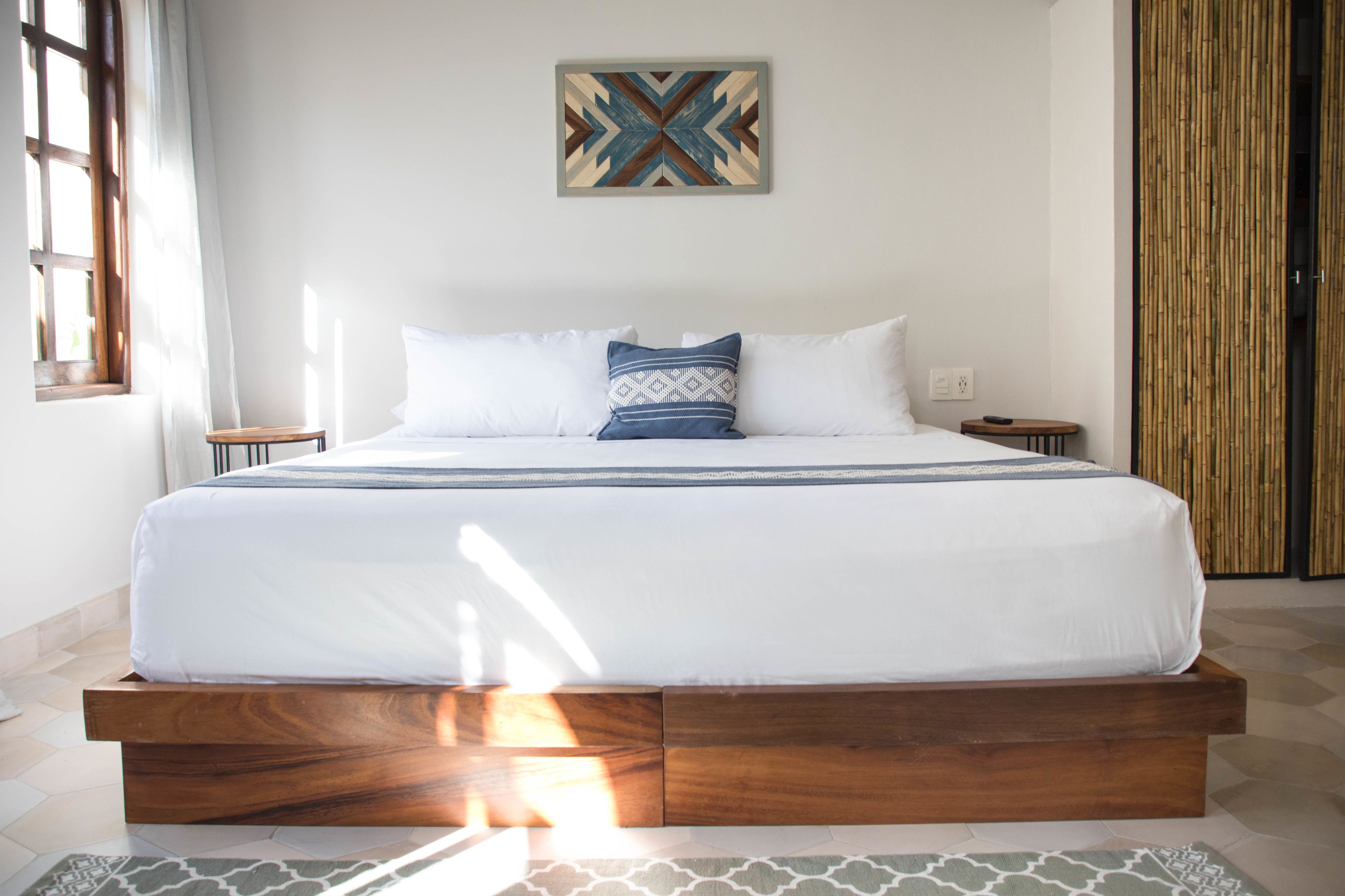 A modern bedroom with a wooden platform bed, white bedding, and a geometric wall art piece.