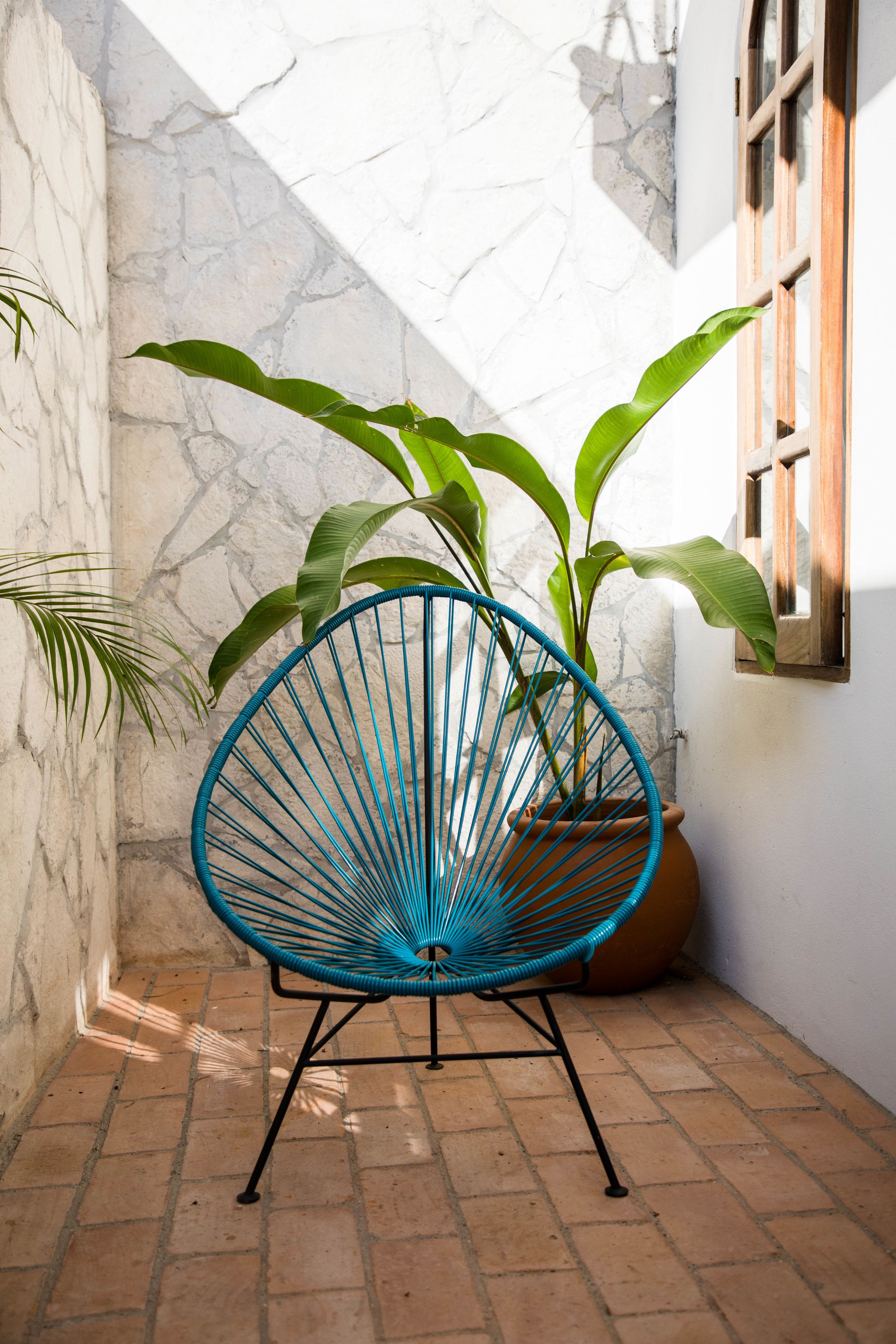 A blue chair with a woven backrest, a potted plant, and a stone wall.
