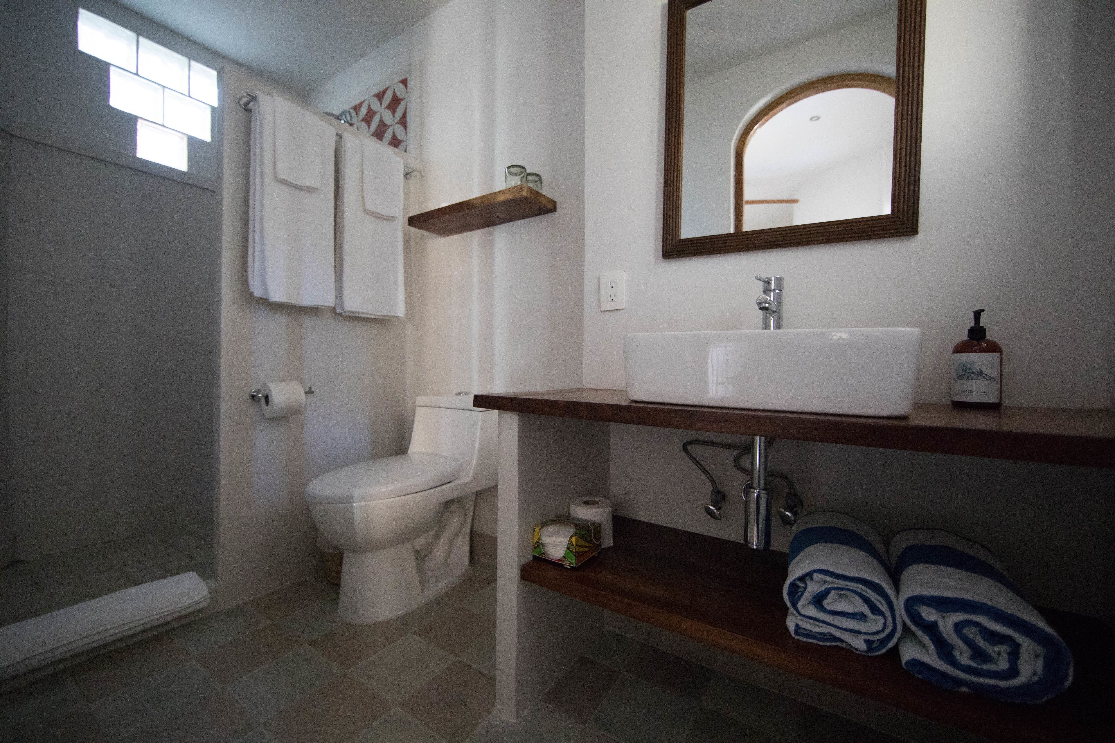 Baño con inodoro, lavamanos y ducha. Hay toallas y un dispensador de jabón en la encimera.