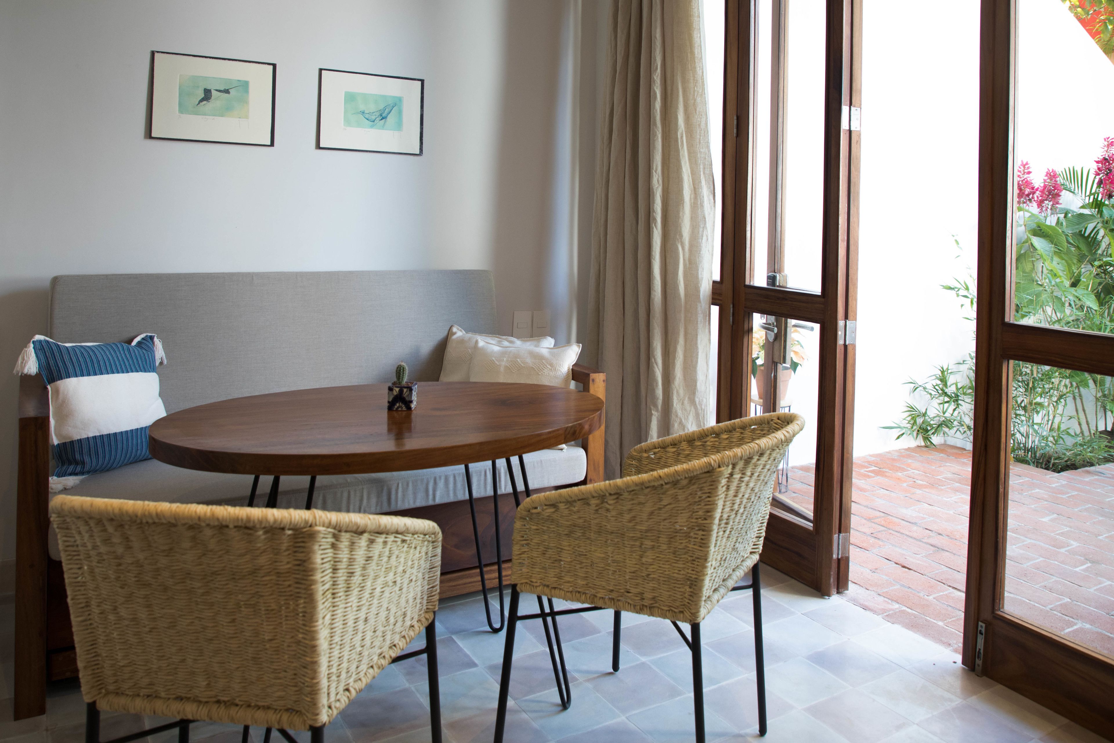 A room with a round wooden table, two wicker chairs, a grey sofa, and two framed pictures on the wall.