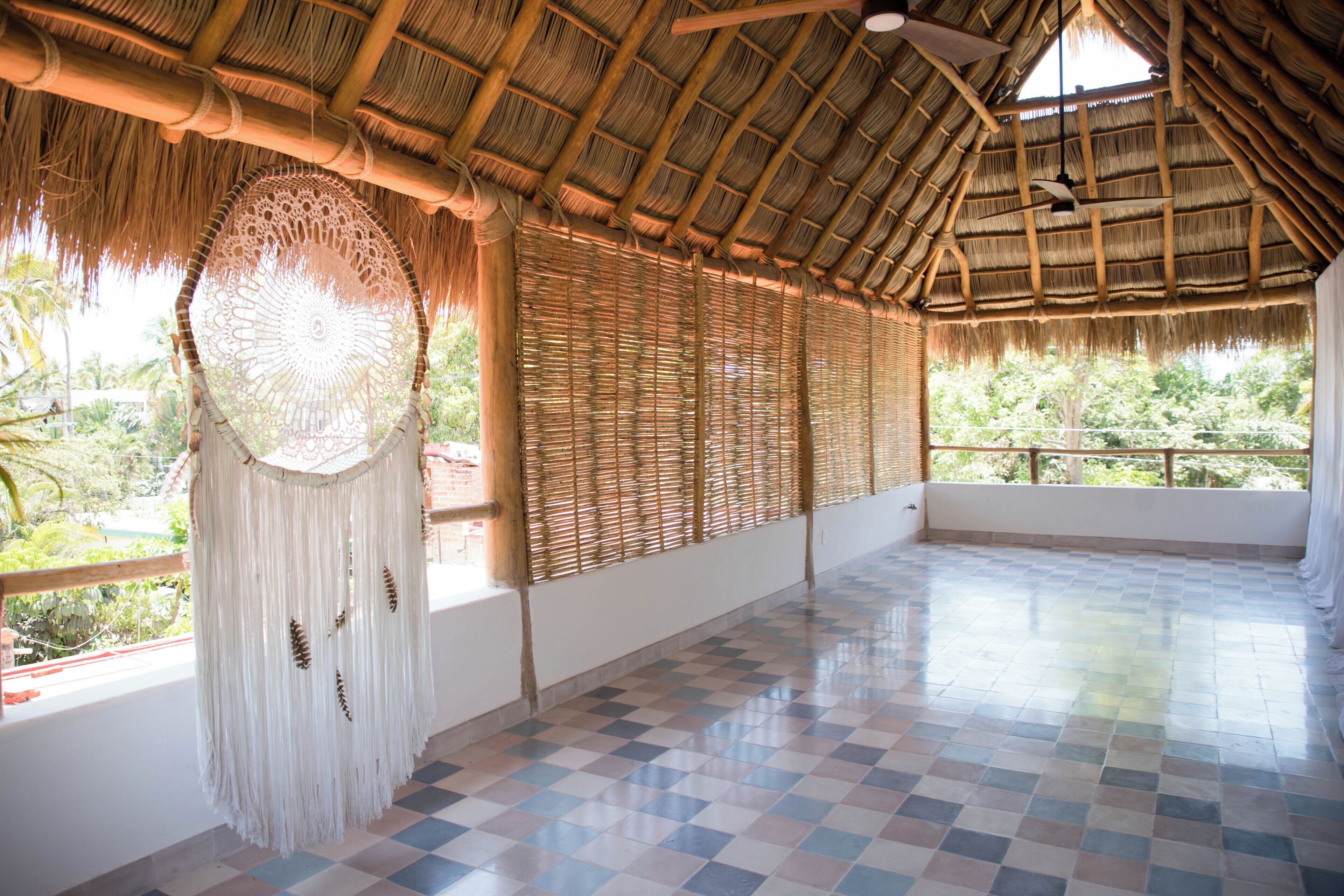 Amplia habitación con piso a cuadros, techo de paja y un ventanal que da a la vegetación.