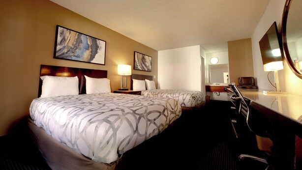 A hotel room with two beds, a desk, a chair, a TV, and artwork on the walls.