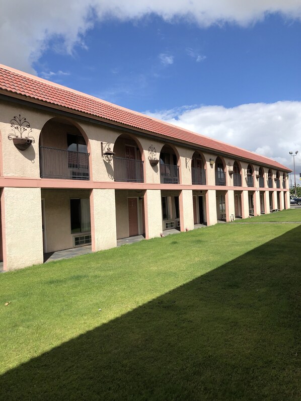 A row of motel rooms with individual balconies, a red-tiled roof, and a well-maintained lawn.