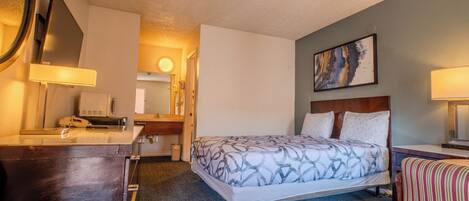 A hotel room with a bed, a desk, a chair, a mirror, and a painting on the wall.