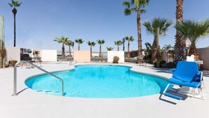 A swimming pool with a blue water feature, surrounded by palm trees and a clear sky.