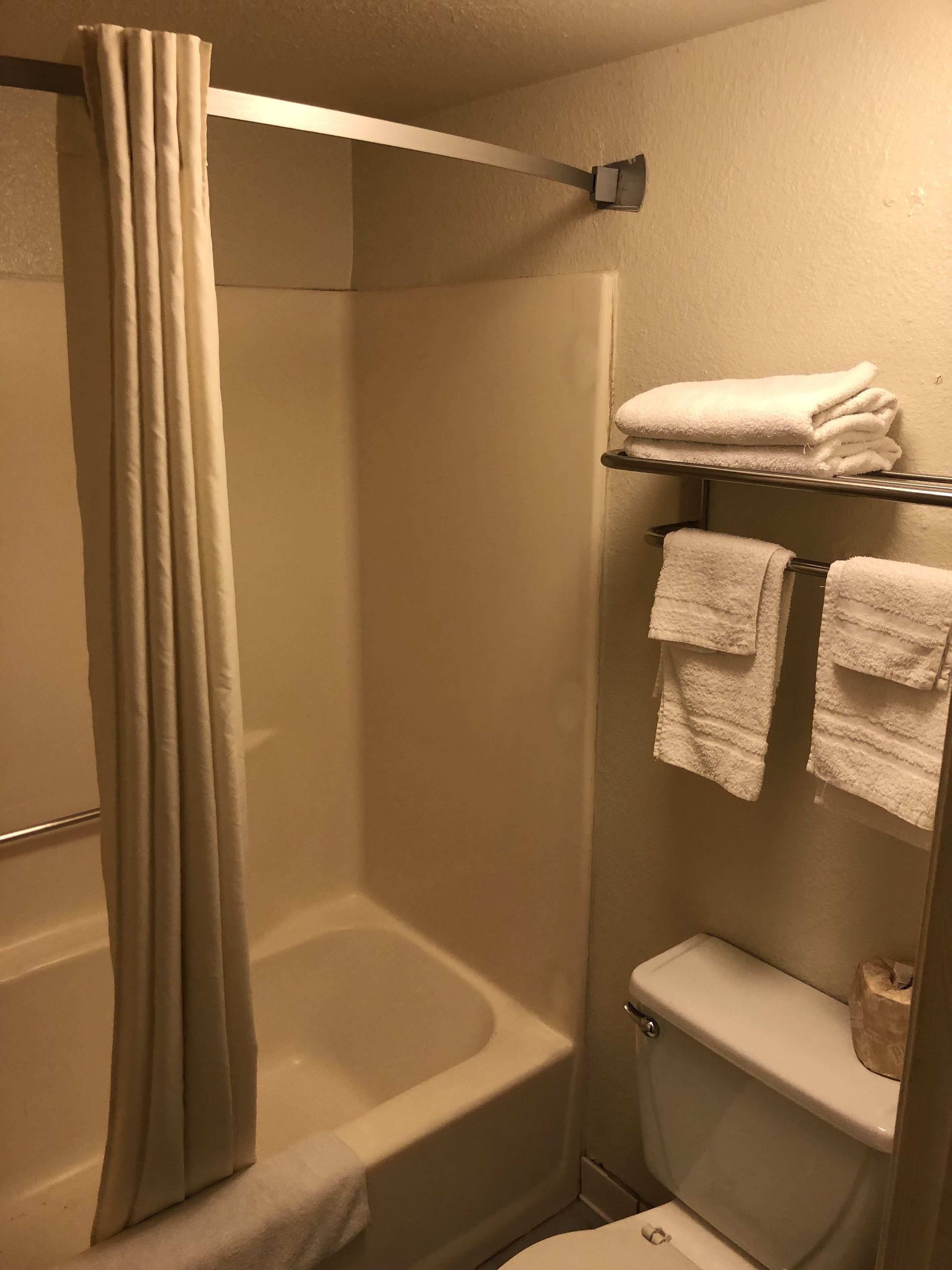 Un baño con cortina de ducha, bañera, inodoro y un perchero con toallas dobladas.