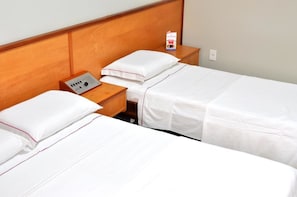 A hotel room with two single beds, a wooden headboard, a bedside table with a radio, and a wall socket.