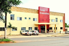 A hotel named 'Hotel Executivo' with a red sign, a yellow facade, and a parking area with several cars.