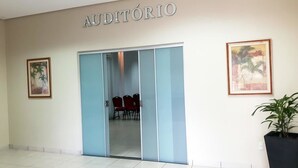 An interior with a sign reading "AUDITÓRIO" above a glass door leading to a room with red chairs. - Hotel Executivo (Araguaina)