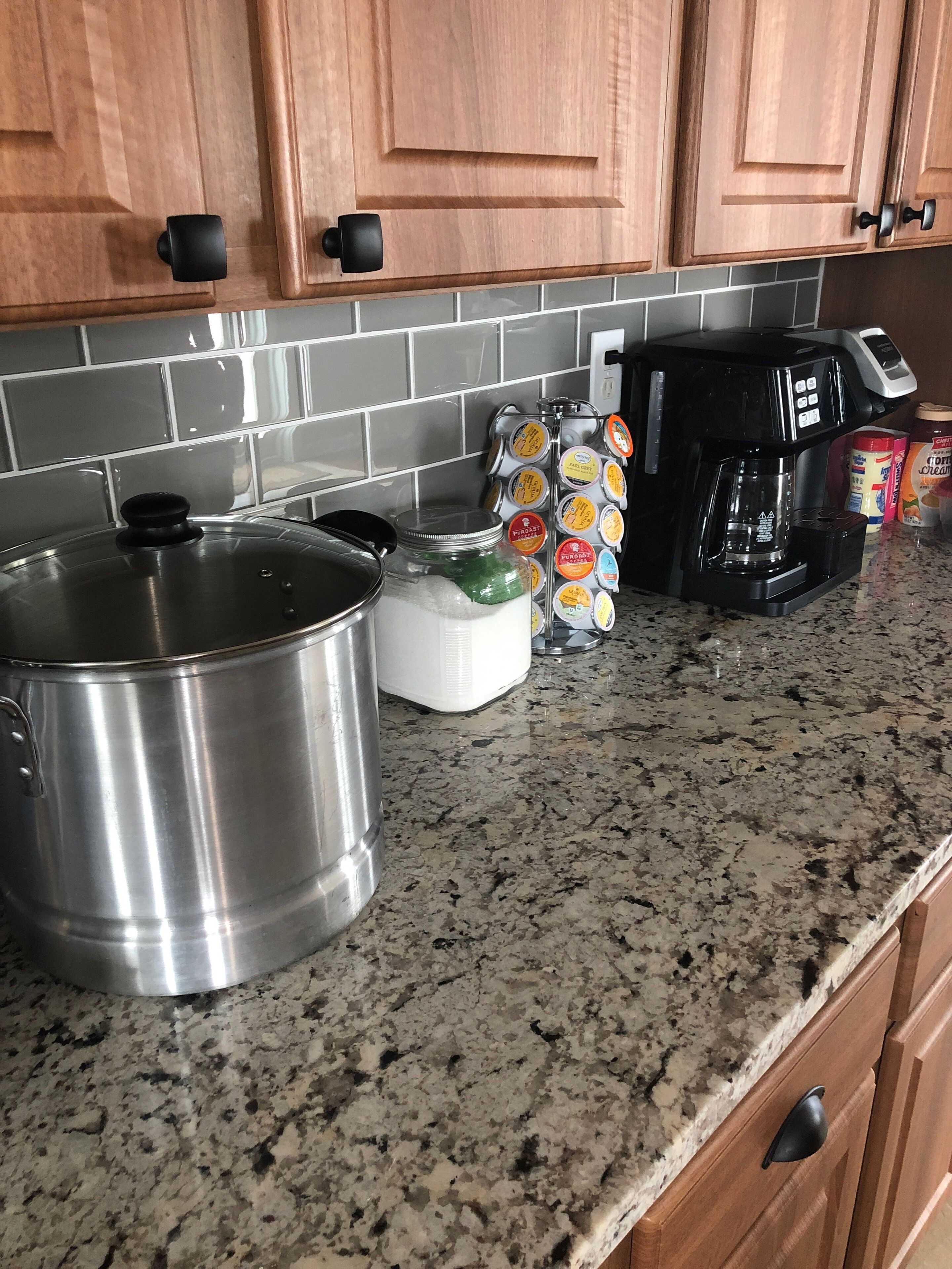 A kitchen with granite countertops, stainless steel cookware, a coffee maker, and a spice rack.
