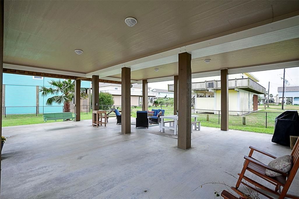 An outdoor covered patio area with concrete flooring, wooden pillars, and outdoor furniture including a table and chairs.