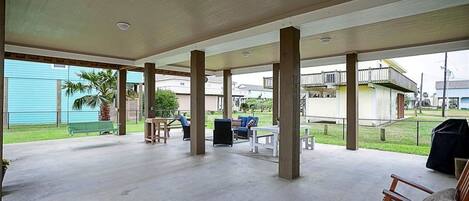 An outdoor covered patio area with concrete flooring, wooden pillars, and outdoor furniture including a table and chairs.
