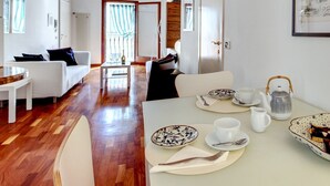 Een moderne woonkamer met een houten vloer, witte meubels en een eethoek met een gedekte tafel voor thee.
