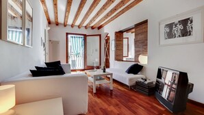 Een moderne woonkamer met houten balken, een witte bank, een klein tafeltje en een televisie.
