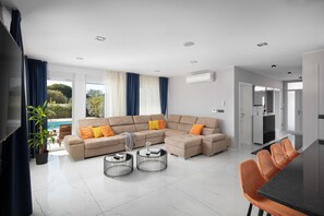Un salon moderne avec un canapé d’angle, deux tables basses et un coin repas doté de chaises orange.