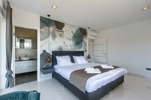 Une chambre moderne avec un grand lit, une armoire intégrée et une salle de bain visible à travers une porte ouverte.
