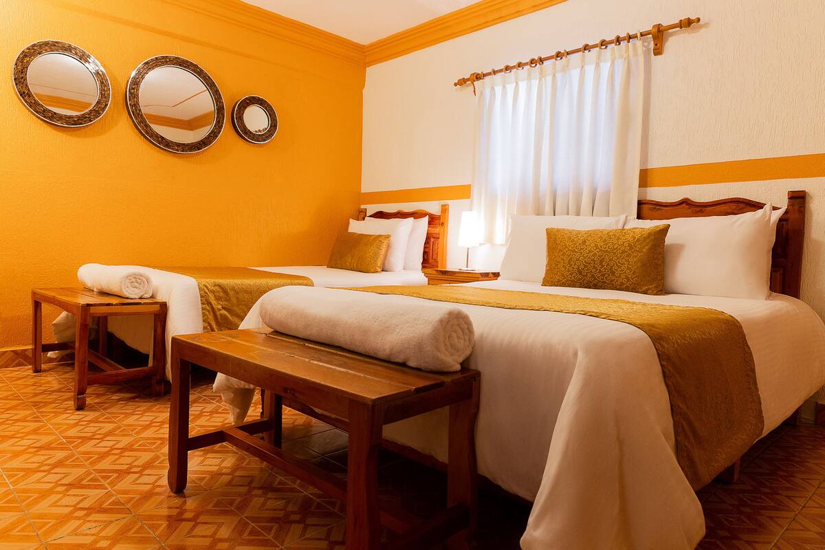 A hotel room with two beds, a wooden bench, and a small table.