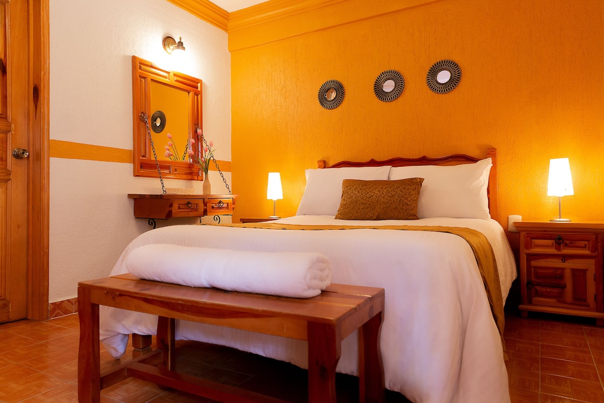 A hotel room with a bed, bedside tables, a nightstand, a mirror, and wall decor.