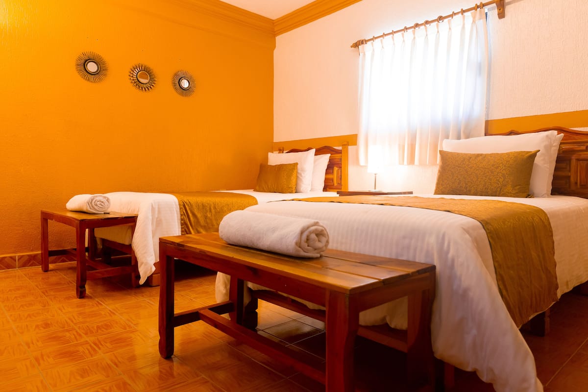A hotel room with two beds, a wooden bench, and a small table.