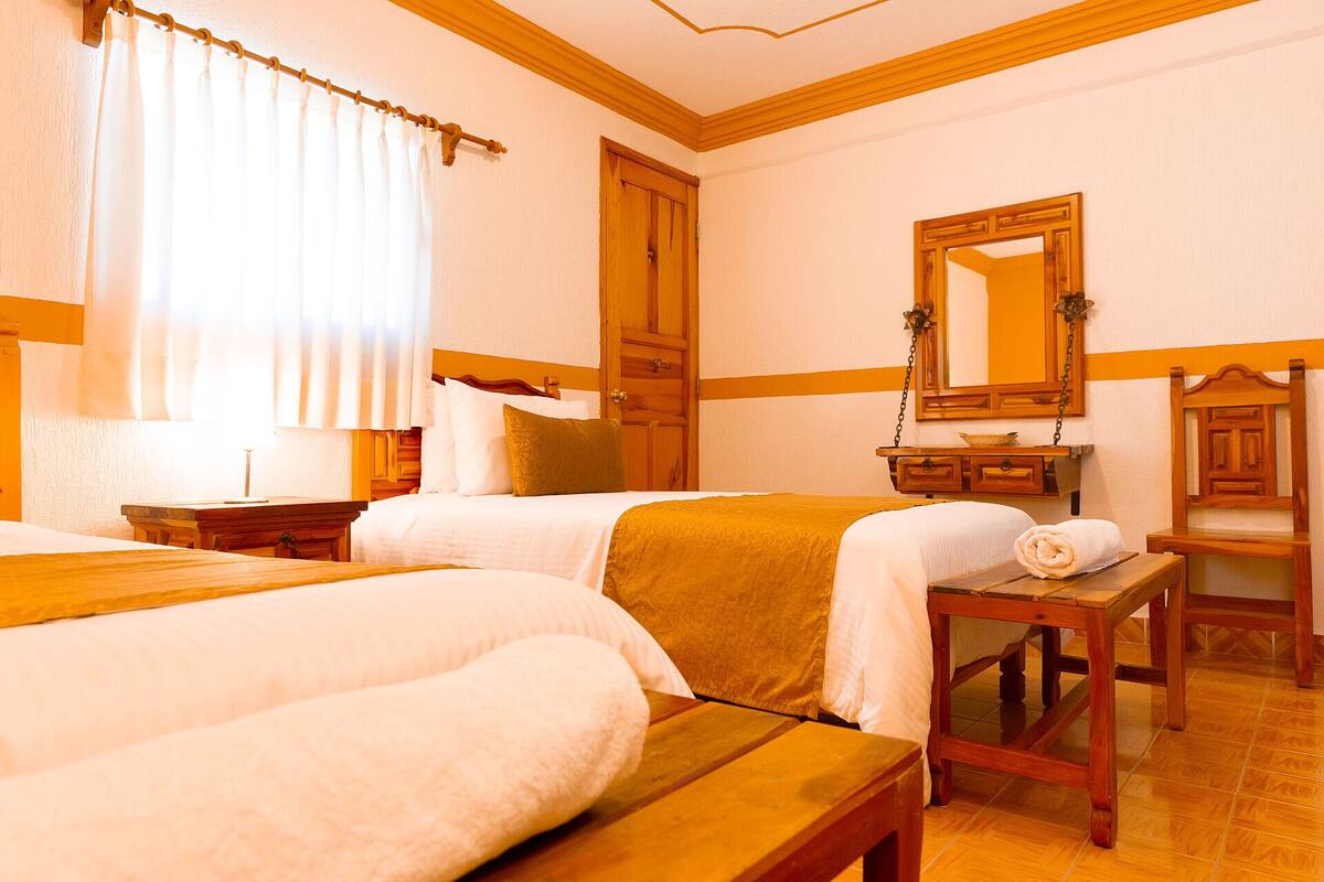 A hotel room with two beds, a wooden dresser, a mirror, and a window with curtains.