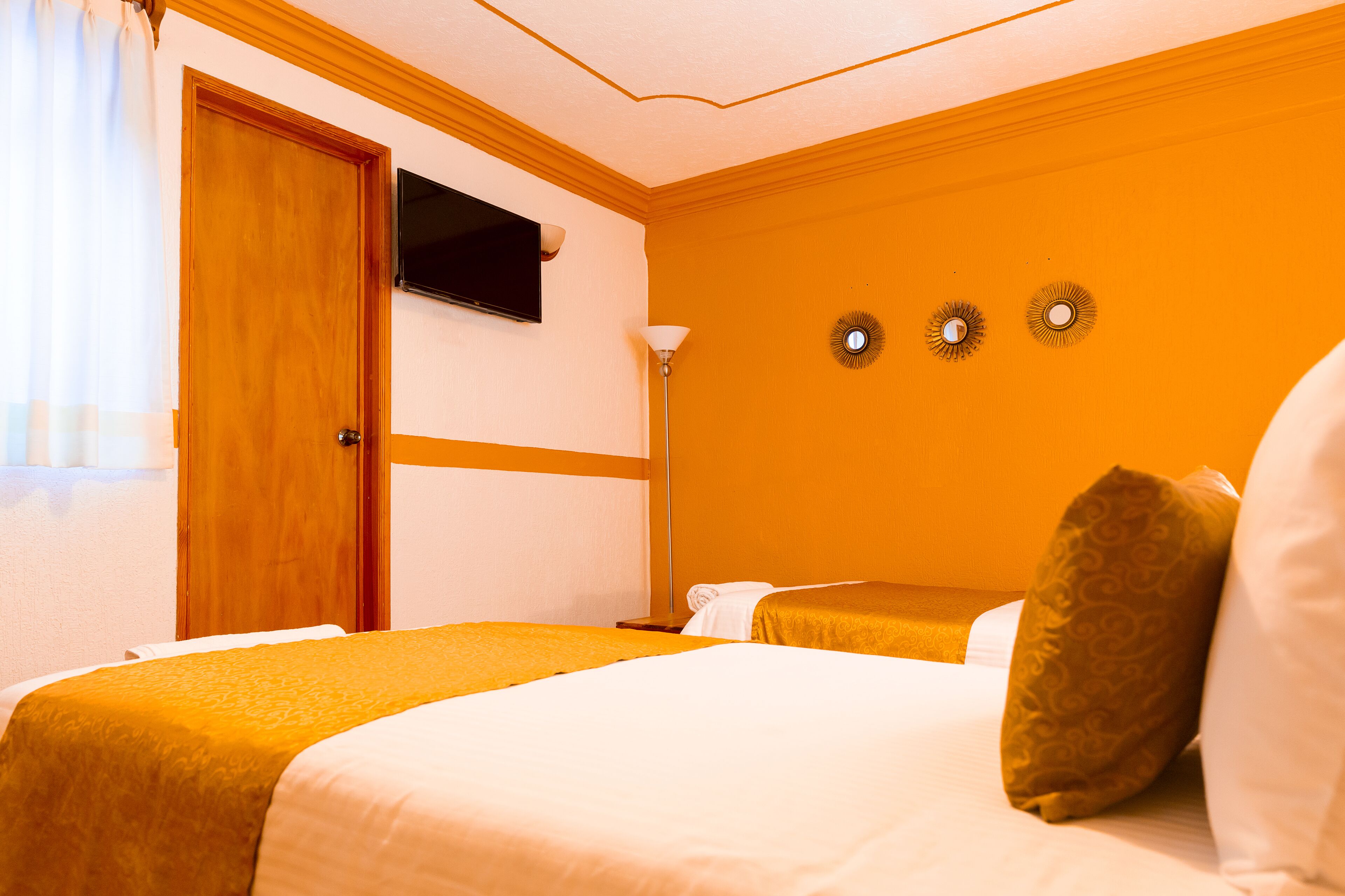 Habitación de hotel con cama, televisión y lámpara de pared.