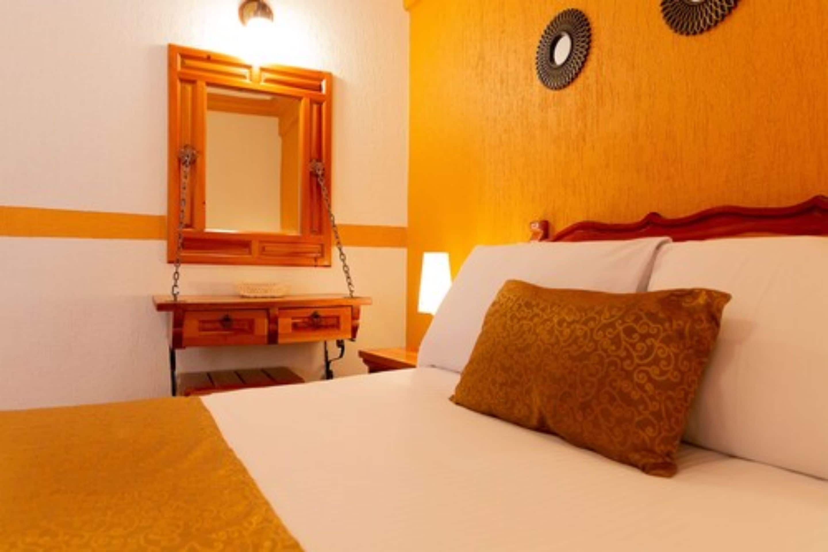 Een hotelkamer met een bed, nachtkastje, spiegel en een wandlamp.