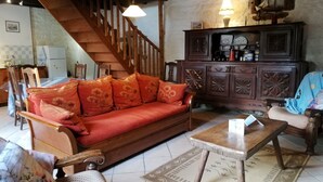 Una sala de estar acogedora con una escalera de madera, un sofá rojo, un aparador de madera y un comedor con sillas y una mesa.