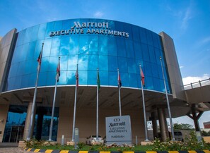 A Marriott Executive Apartments building with a modern glass facade, multiple flags, and a sign indicating its name and location. - Marriott Executive Apartments Madinah (Madinah)