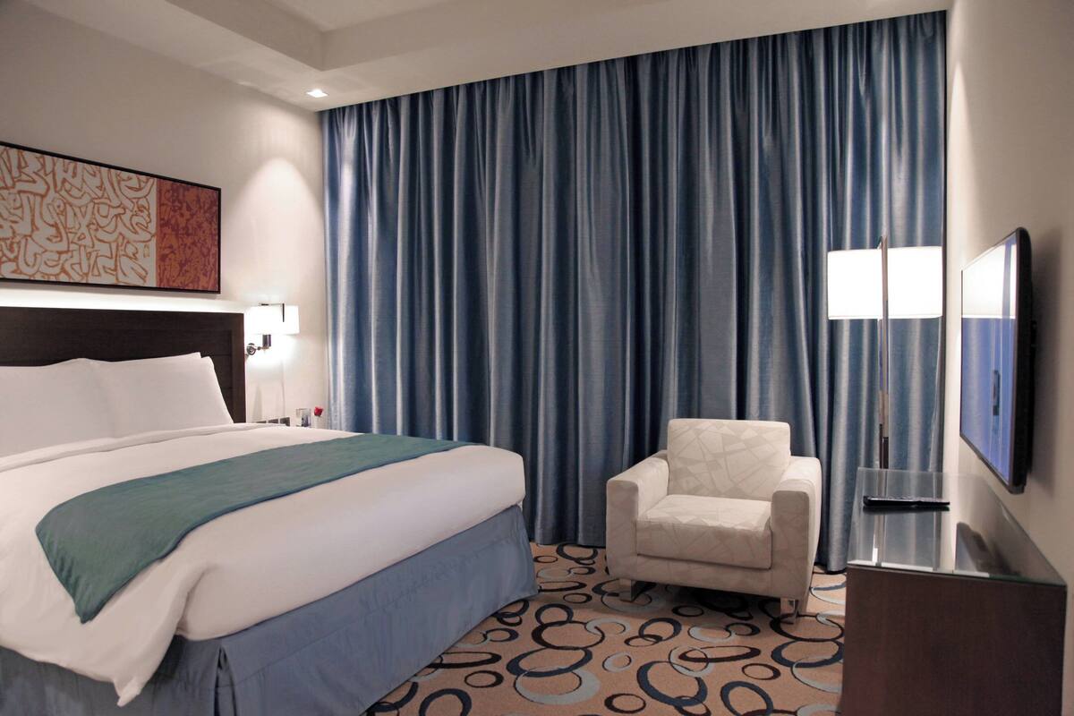 A hotel room with a large bed, a chair, a TV, and a curtain.