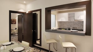 Quarto de hotel moderno com área de refeições, cozinha com uma janela grande e um espelho refletindo o ambiente.