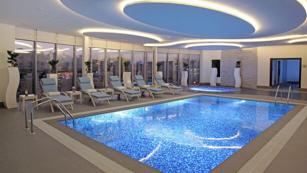 Piscina interior moderna com espreguiçadeiras e vista para a cidade.