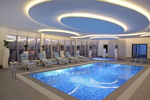 Une piscine intérieure moderne, dotée de chaises longues et offrant une vue sur la ville.