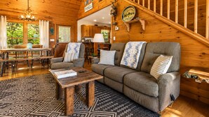 A wooden cabin interior with a dining area, a sofa set, a staircase, and a welcome sign. - Call of the Wild, Blue Ridge, GA (Morganton)