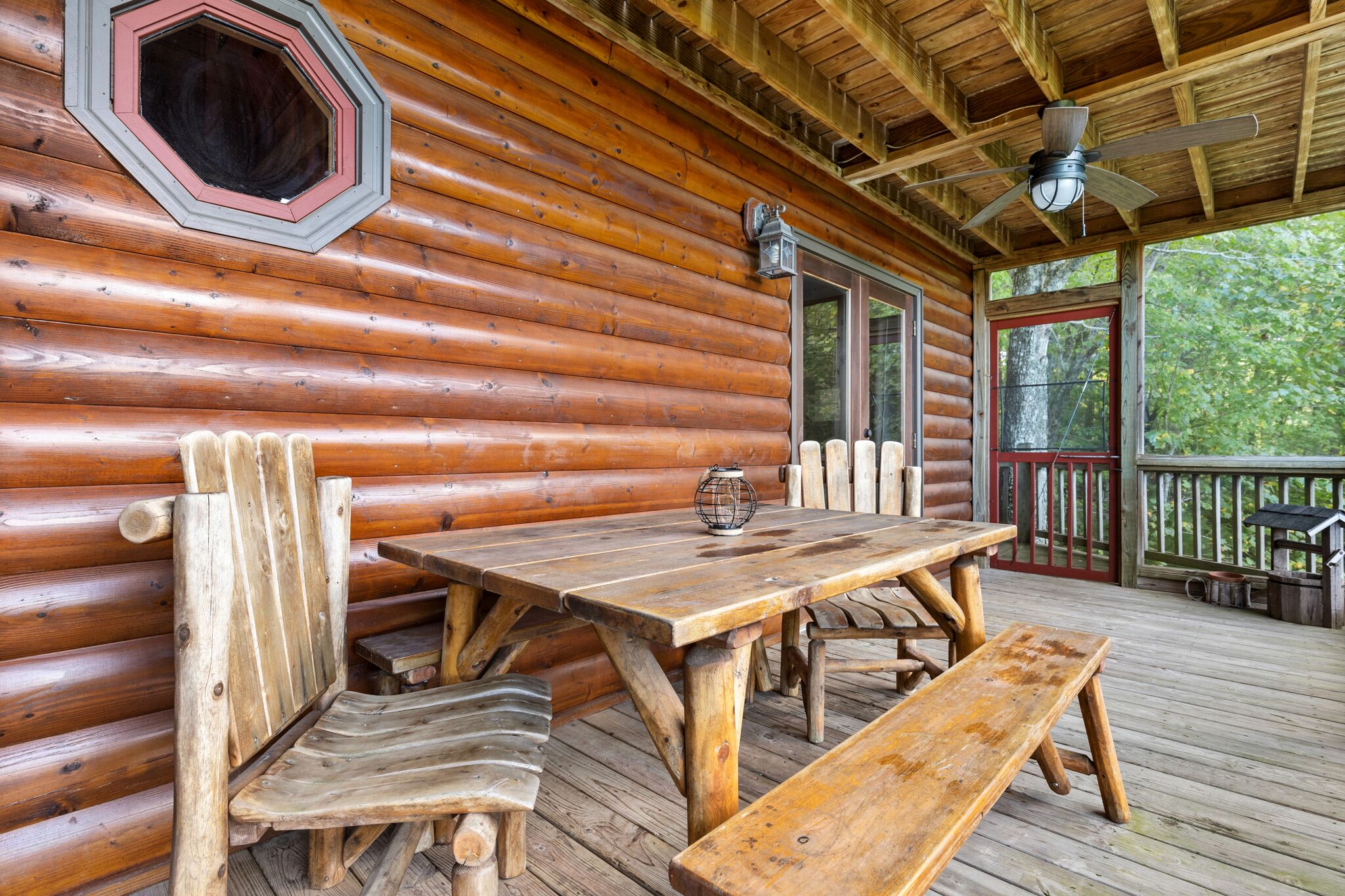 A wooden cabin with a large dining table, benches, and a ceiling fan.
