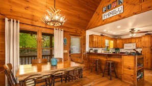 A wooden cabin interior with a dining table, chairs, a chandelier, a kitchen with wooden cabinets, and a sign that reads 'RUM Family.' - Call of the Wild, Blue Ridge, GA (Morganton)
